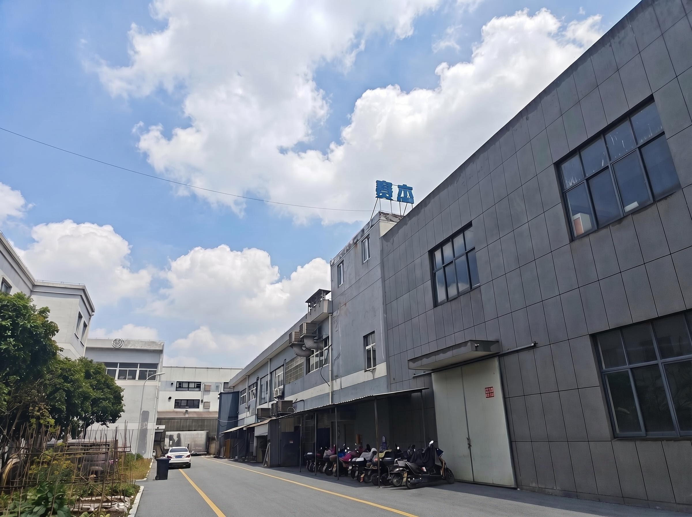 Modern factory exterior view, gray building with blue glass curtain wall, surrounded by greenery, reflecting company size and modernization level